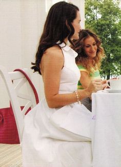 two women sitting at a table talking to each other in front of a white chair
