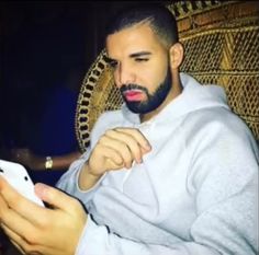 a man sitting in a chair holding a cell phone and looking at the screen with his hand