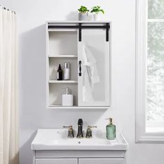 a white bathroom sink sitting under a mirror next to a window with plants on it