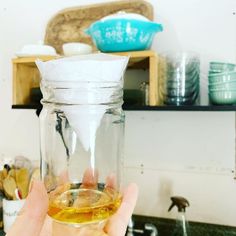 a person holding up a glass jar filled with liquid on top of a kitchen counter