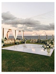 an outdoor wedding setup with white flowers and draping on the grass near the ocean