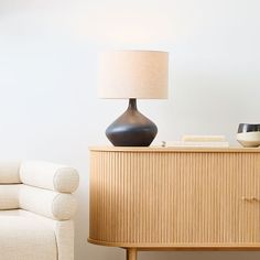 a living room with a white couch and a wooden cabinet next to a lamp on a table