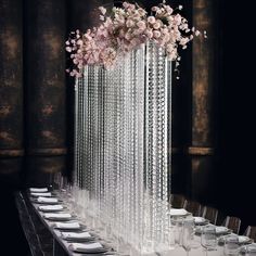 a long table with plates and wine glasses on it in front of a tall floral centerpiece