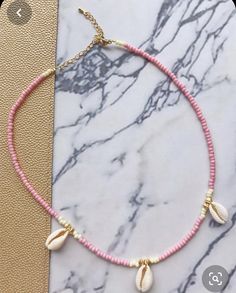 a pink beaded necklace with seashells on it and a gold plated charm