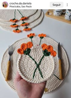 a hand is holding a crocheted plate with orange flowers on it and two forks