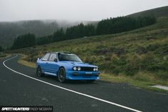 a blue car parked on the side of a road next to a lush green hillside