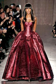 a model walks the runway in a red gown with sequins on it's skirt