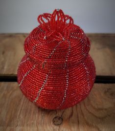 a red beaded basket sitting on top of a wooden table next to a wall