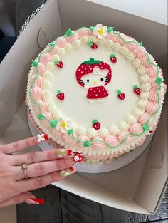 a hello kitty cake in a box with someone's hand next to the cake