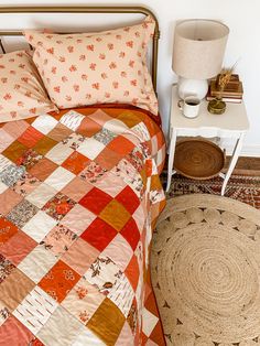 a bed with an orange and white quilt on top of it next to a rug