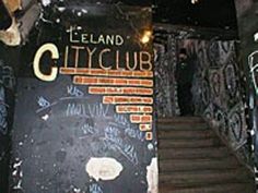 the stairs lead up to an underground club with graffiti on it's walls and below them is a chalkboard sign that reads, leland city club