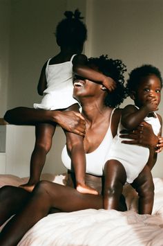 two women and a child sitting on a bed with their arms around each other's shoulders