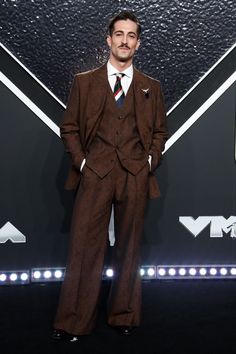 a man in a suit and tie standing on a black carpet with his hands in his pockets