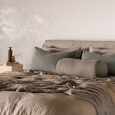 a bed with pillows and blankets on it in front of a white wall, next to a vase