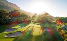 an aerial view of a golf course with the sun shining on it and trees in the foreground