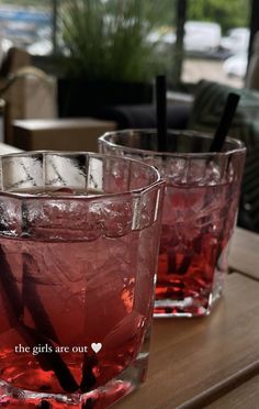 two glasses filled with red liquid sitting on top of a wooden table next to each other