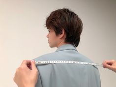 a man is measuring his shirt with a tape on the back of his jacket and he's holding it in one hand