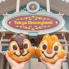 two people holding up some food in front of a disney land sign with chippy faces on it