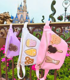 three purses are hanging on a fence in front of a castle with flowers and trees