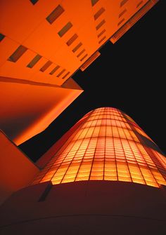 a tall building lit up at night with orange lights on it's side and the sky in the background