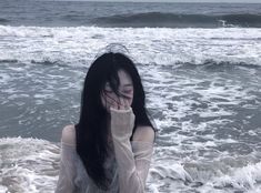 a woman with long black hair standing in the ocean