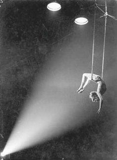 a man hanging upside down in the air with a light shining on him and two people below