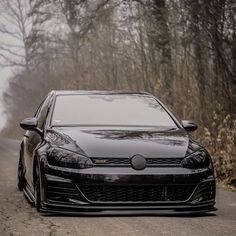 a black car parked on the side of a road in front of trees and bushes