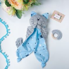 a stuffed cat laying on top of a blue blanket next to a flower bouquet and pacifier