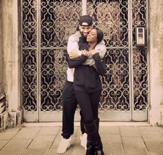 a man and woman hugging each other in front of an iron gated entrance to a building