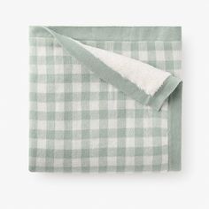 a green and white checkered blanket folded on top of a bed with a pillow