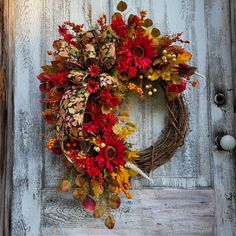 a wreath is hanging on a door with autumn leaves and berries around it in front of an old wooden door