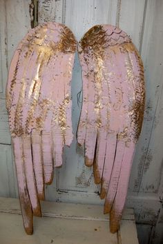 two pink and gold angel wings sitting on top of a wooden table next to a white door