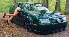 a woman leaning on the door of a green car with her legs hanging over it