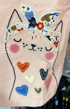 a close up of a person wearing a pink shirt with an embroidered cat on it