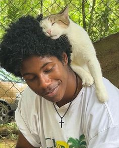 a cat sitting on top of a man's head in front of a fence