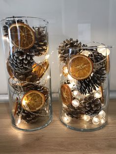 two glass vases filled with pine cones and orange slices