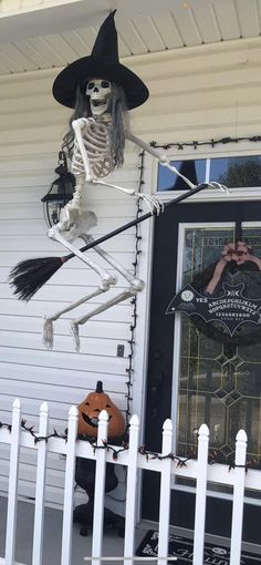 a skeleton hanging from the side of a house with a broom and hat on it's head