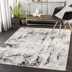 a white and black area rug in a living room with a chair, table and potted plant