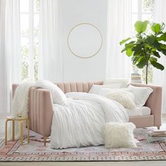 a living room with a pink couch, white pillows and a potted plant in the corner
