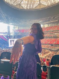 a woman in a purple dress is holding her hand out to the crowd at a sporting event