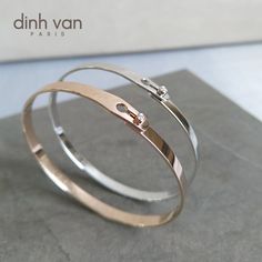 two silver and gold bracelets on top of a gray surface with the words, dinh van paris