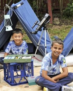 two young boys sitting on the ground in front of some tents with lights and camera equipment