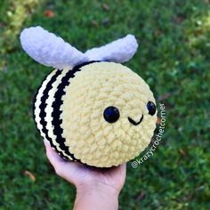 a hand holding a small stuffed animal with a bee on it's head in the grass