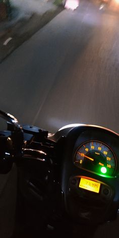 the dashboard of a motorcycle on a city street at night, with lights from headlights