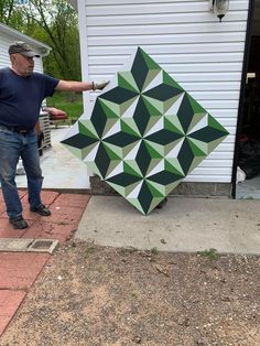 a man is holding up a large green and white geometric design on the side of a house