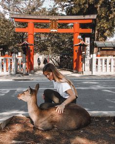 a woman sitting on the ground next to a deer in front of an orange gate