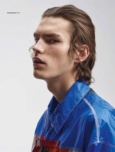 a young man with long hair wearing a blue shirt and red pants, looking off to the side