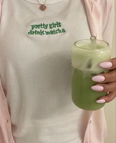 a woman holding a green drink in her right hand and wearing a white shirt with the words pretty girls drink matcha on it