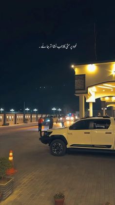 a white truck is parked in front of a gas station at night with two men standing next to it