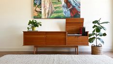 a painting hanging on the wall above a wooden cabinet with books and plants in front of it